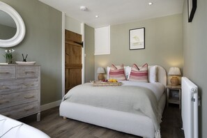 A bedroom with a bed, bedside tables, a dresser, a mirror, and a framed picture on the wall. - 4 Wraggs Row -  a cottage that sleeps 6 guests  in 3 bedrooms (Stow-on-the-Wold)