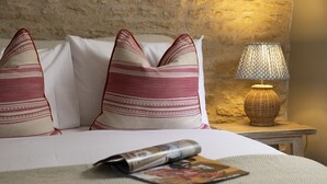 Una cama con dos almohadas, una revista y una lámpara en la mesita de noche.