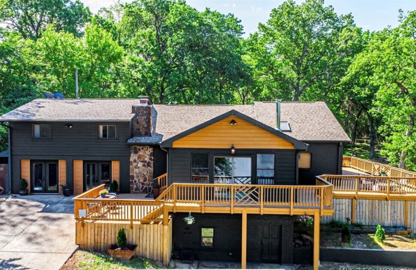 Une maison à deux étages avec une cheminée en pierre, une terrasse en bois et des fondations en pierre.