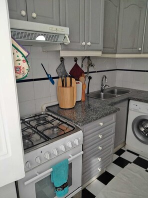 A compact kitchen with a gas stove, oven, sink, and a washing machine. - Apartment near Feira da Ladra & Alfama (Lisboa)