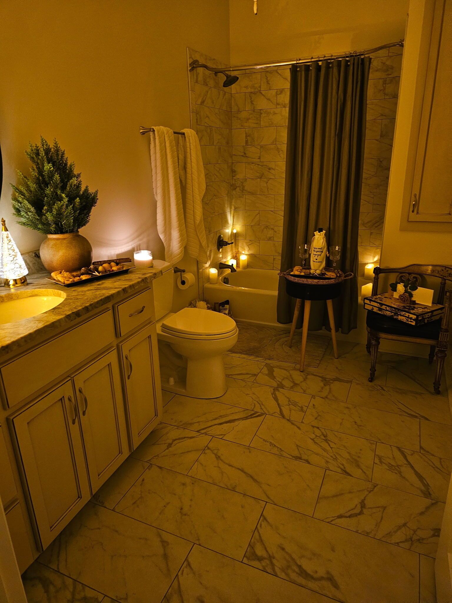 A bathroom with a marble floor, a bathtub, a toilet, a sink, and a small table with a plant.