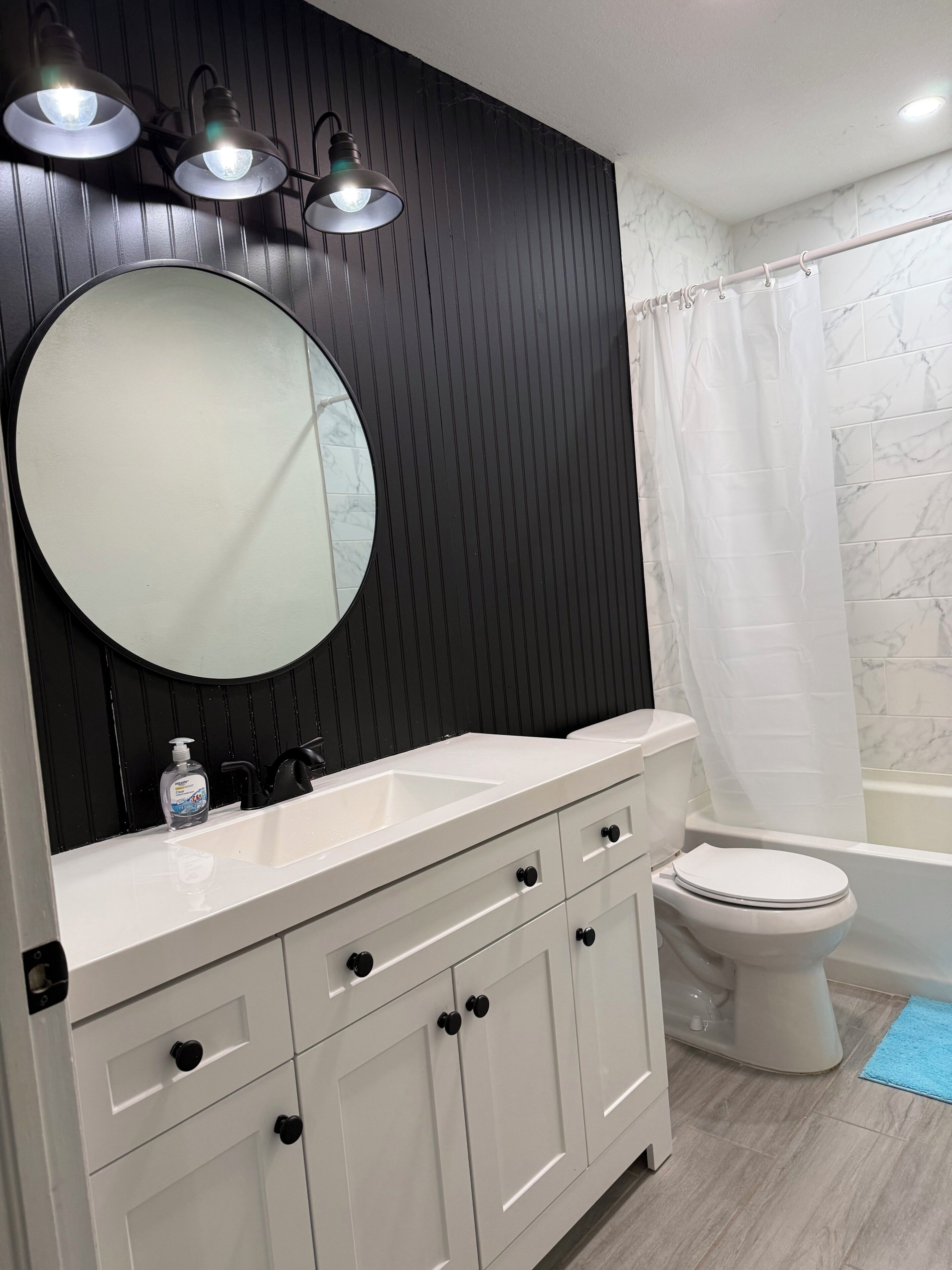 A bathroom with a white vanity, a round mirror, a toilet, and a bathtub.