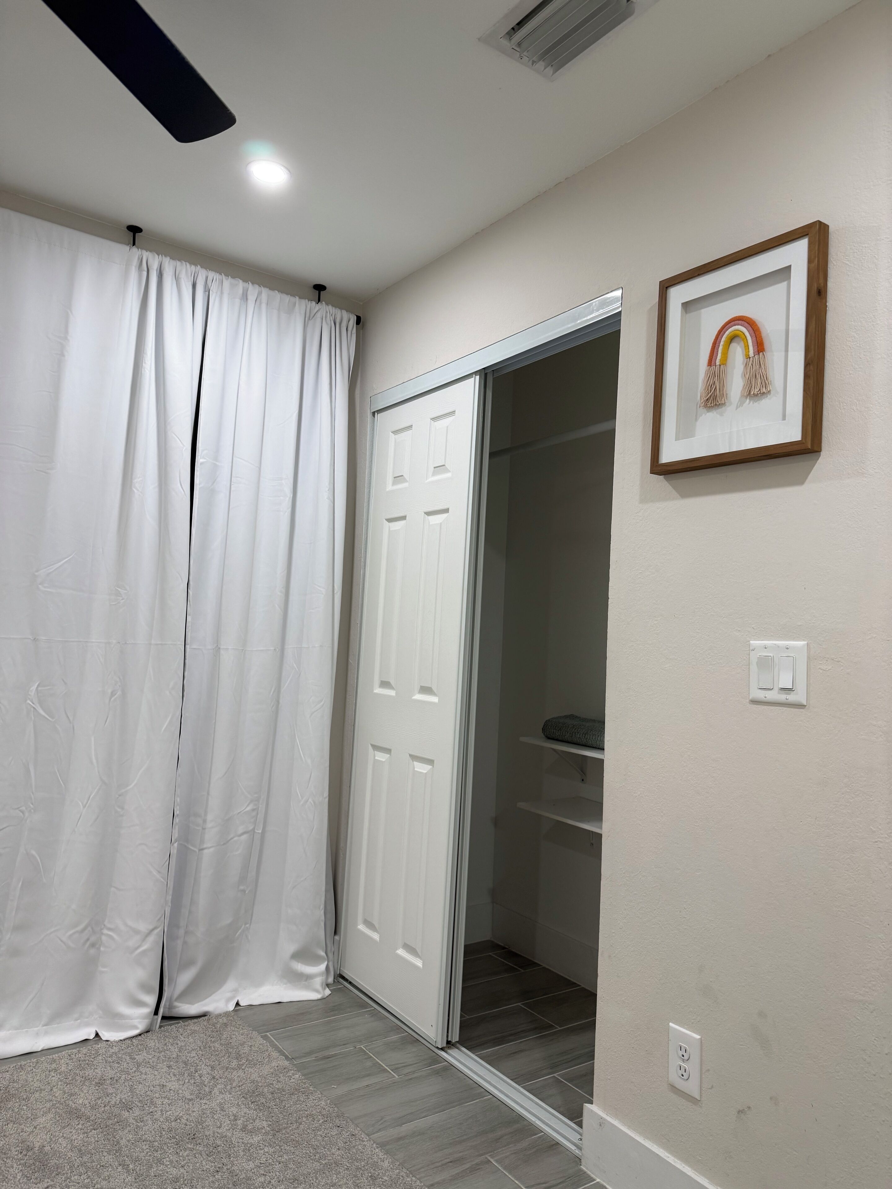 A room with a white door, a white curtain, a framed picture on the wall, and a ceiling fan.