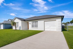 Une maison d’habitation à un étage, avec une façade blanche, un toit gris et un garage.