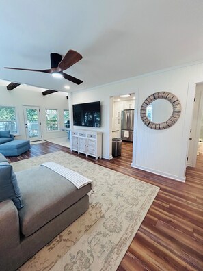 A spacious living room with a large sofa, a flat-screen TV, and a ceiling fan. - The Tree House (Atlantic Beach)