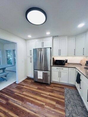 A modern kitchen with white cabinets, a stainless steel refrigerator, and a patterned rug. - The Tree House (Atlantic Beach)