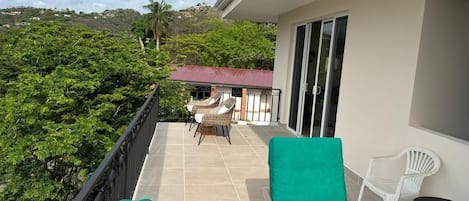A balcony with a view of a red-roofed building, a table with chairs, and a potted plant.