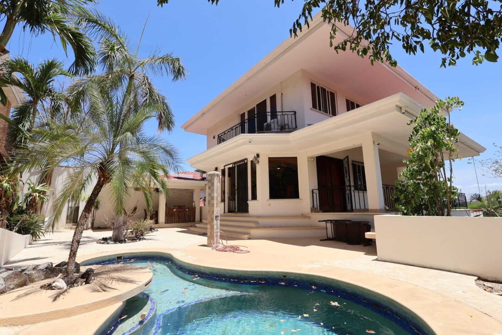 Uma casa de dois andares com piscina, palmeiras e uma varanda.