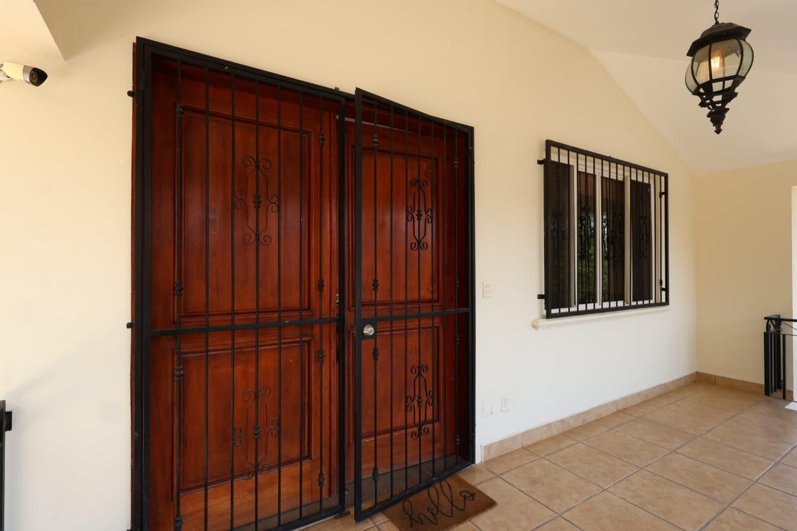 A hallway with a large wooden door and a window with metal bars.