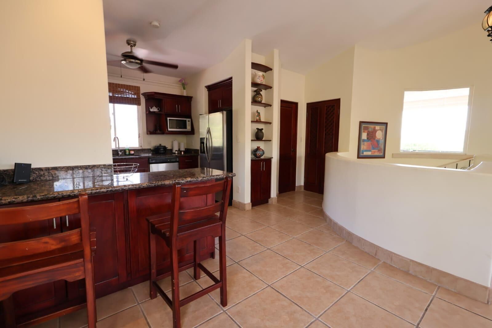 A kitchen with a granite countertop, wooden cabinets, a microwave, and a refrigerator.