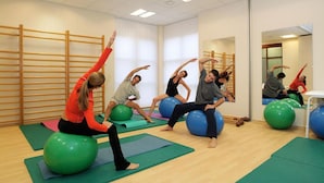 A group of people exercising on exercise balls in a room with wooden slats on the walls and a large mirror. - Svoboda Ensana Health Spa Hotel (Marianske Lazne)