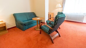 A hotel room with a green patterned sofa, a wooden chair, a small round table, and a lamp. - Svoboda Ensana Health Spa Hotel (Marianske Lazne)
