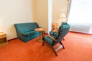 A hotel room with a green patterned sofa, a wooden chair, a small round table, and a lamp. - Svoboda Ensana Health Spa Hotel (Marianske Lazne)