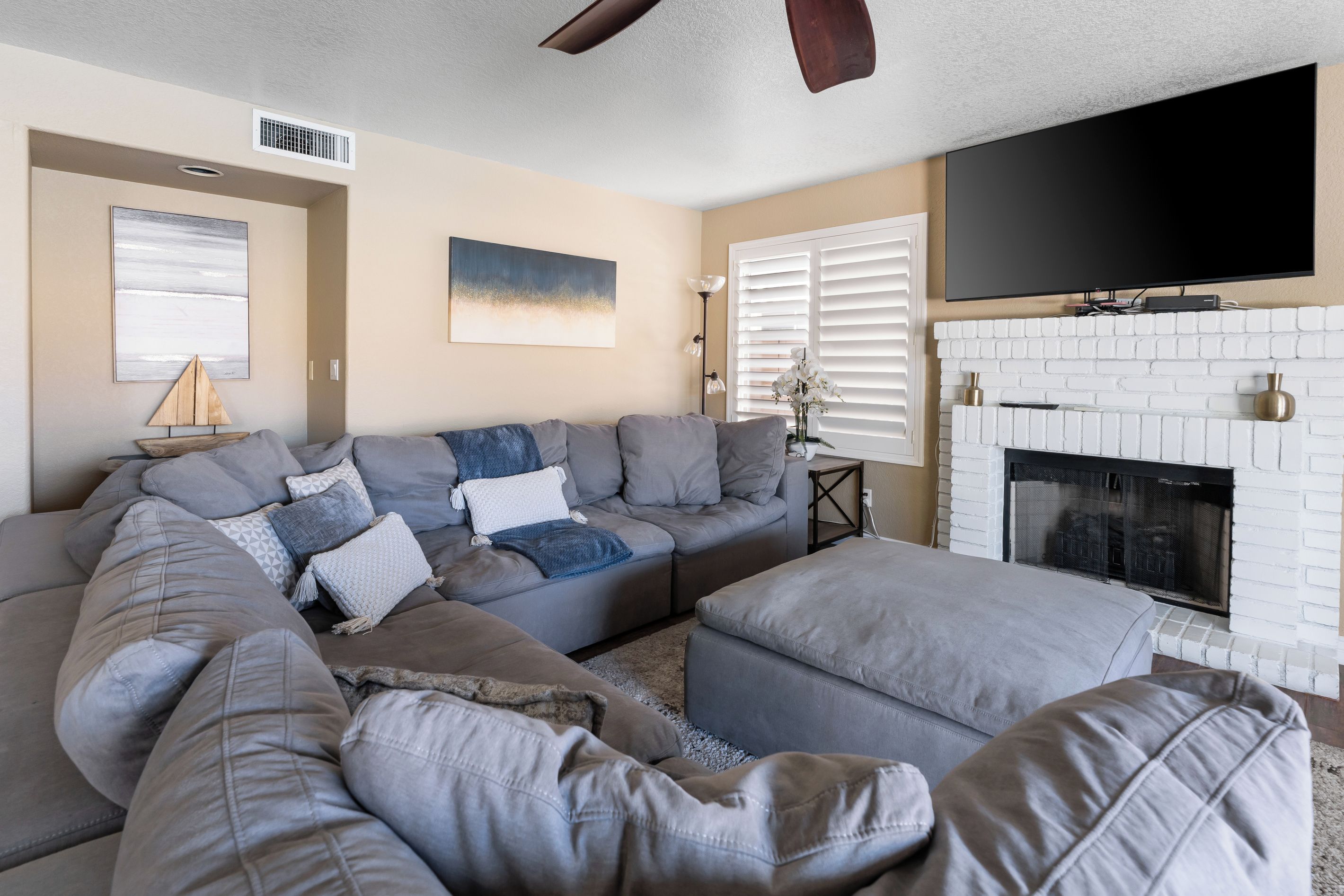 A living room with a sectional sofa, ottoman, fireplace, television, and artwork on the walls.