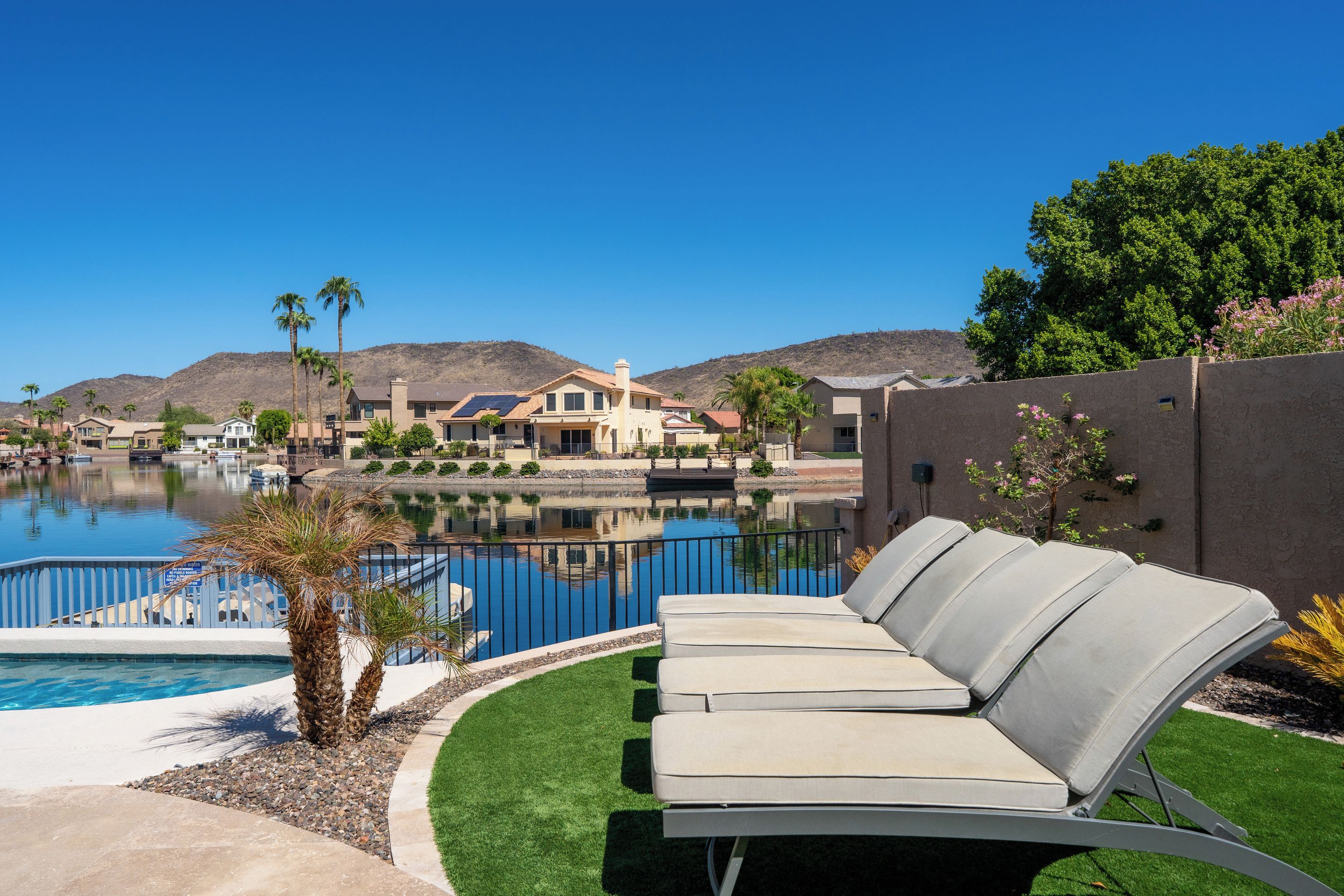A residential area with a swimming pool, lounge chairs, and a view of a hill.