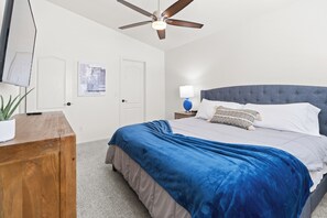 A bedroom with a bed, a ceiling fan, a bedside table with a lamp, and a wall-mounted artwork. - Lakefront Retreat | Free Heated Pool + Game Room (Glendale)