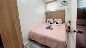 Ein Schlafzimmer mit Bett, Nachttisch, Fenster mit Jalousien, Klimaanlage und Tür.