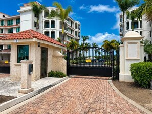 A gated entrance with a paved driveway leading to a building with a tiled roof and multiple balconies. - Luxury Oceanview Condo | Hyatt PR Golf & Beach (Rio Grande)