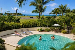 A pool area with lounge chairs, a pool, palm trees, and a view of the ocean. - Luxury Oceanview Condo | Hyatt PR Golf & Beach (Rio Grande)