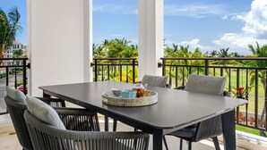 En balkon med et bord og stole, udsigt til palmer og en bygning i baggrunden.