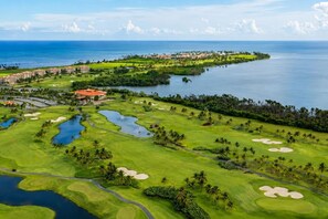 Un parcours de golf agrémenté d’obstacles d’eau, de palmiers et offrant une vue sur l’océan.