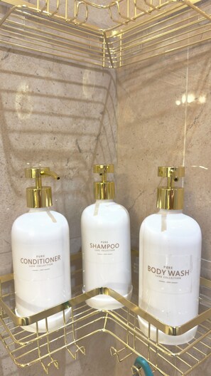Three white bottles with gold pumps on a gold wire shelf against a marble wall.