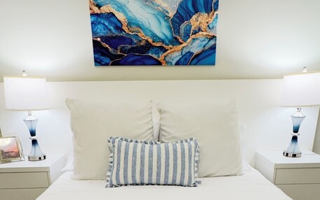 A neatly made bed with a striped pillow and a blue knitted throw.