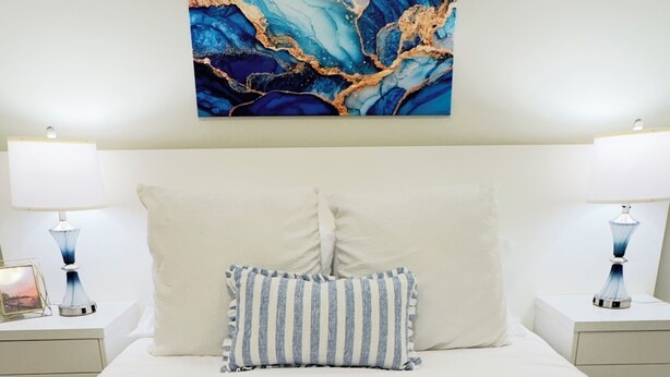 A neatly made bed with a striped pillow and a blue knitted throw.