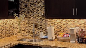 A modern kitchen with dark cabinetry, a tiled backsplash, a granite countertop, and a built-in dishwasher.