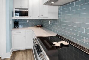Una cocina con armarios blancos, una estufa negra y salpicadero de azulejos azules.