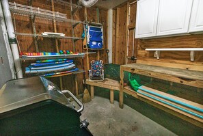 Una habitación con una estantería metálica, una bolsa verde y un banco de madera.