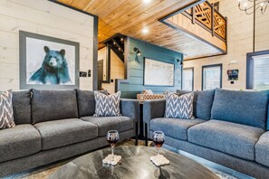 A modern living room with two grey sofas, a coffee table with wine glasses, and a bear painting on the wall. - 8BR/Golf Simulator/FREE Waterpark/PrivatePool (Sevierville)