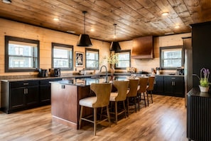 A modern kitchen with a central island, bar stools, wooden flooring, and pendant lighting. - 8BR/Golf Simulator/FREE Waterpark/PrivatePool (Sevierville)