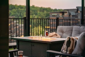 A balcony with a fire feature, a sofa, and a glass table with a drink. - 8BR/Golf Simulator/FREE Waterpark/PrivatePool (Sevierville)