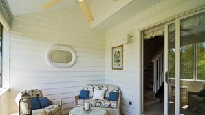 Une véranda couverte, meublée de meubles en osier, dotée d’un ventilateur de plafond et d’une porte-fenêtre coulissante donnant sur un escalier.