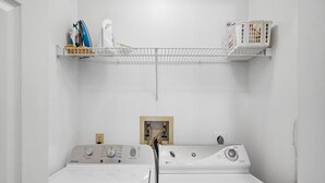 Une buanderie équipée de deux machines à laver Maytag, d’une étagère contenant des produits de nettoyage et d’un mur blanc.