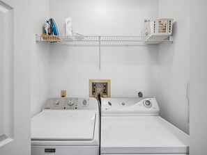 Ein Waschraum mit zwei Maytag Waschmaschinen, einem Regal mit Reinigungsmitteln und einer weißen Wand.