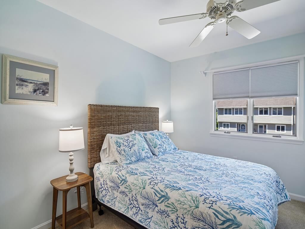 A bedroom with a bed, a ceiling fan, a window with blinds, and a framed picture on the wall.