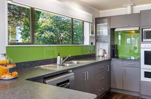 A modern kitchen with a large window, stainless steel appliances, and a green backsplash.