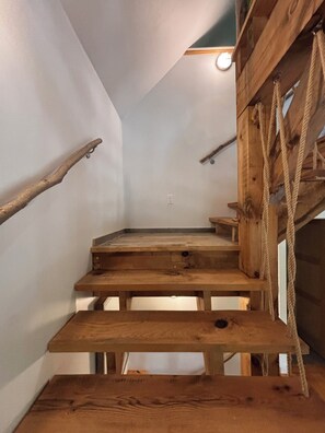 Un escalier en bois au design rustique, doté d’une main courante et d’une échelle en corde.