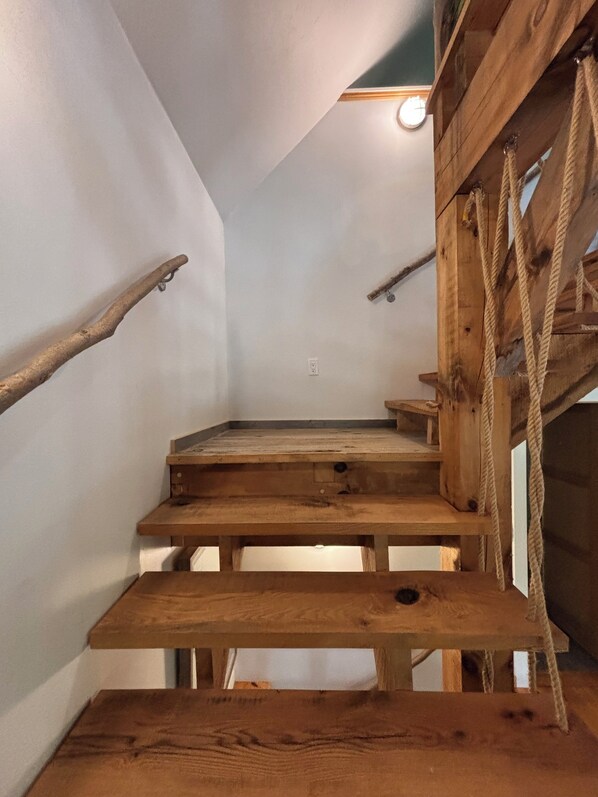 A wooden staircase with a rustic design, featuring a handrail and a rope ladder.