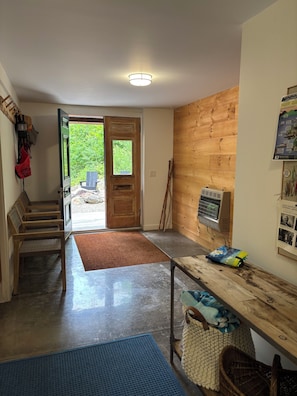 A room with a wooden bench, a table with a cushion, a door leading outside, and a poster on the wall. - New! “Lost on a Mountain in Maine”: Escape to this pond front mountain-retreat! (Lovell)