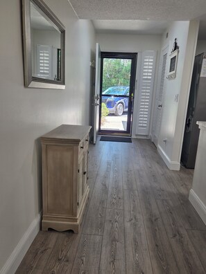A hallway with a wooden cabinet, a door leading outside, and a refrigerator. - First Floor Flat, Surf Court Villa, 2-King Beds, Steps to Coligny Beach! (Hilton Head Island)