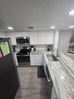 A modern kitchen with white cabinets, stainless steel appliances, and a marble countertop. - First Floor Flat, Surf Court Villa, 2-King Beds, Steps to Coligny Beach! (Hilton Head Island)