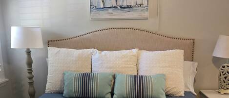 A neatly made bed with a blue quilt, multiple pillows, and two folded towels.