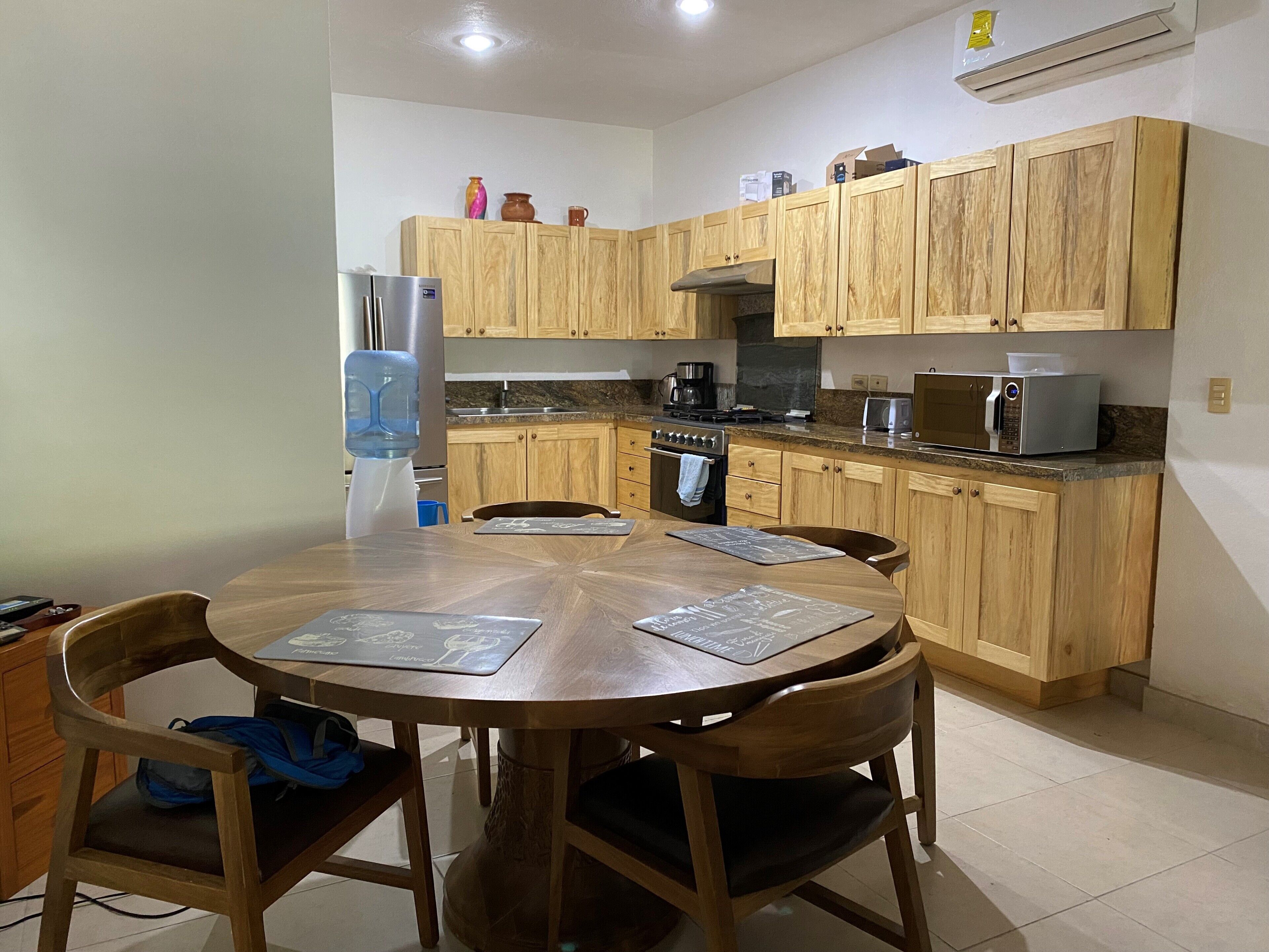 A kitchen with wooden cabinets, a refrigerator, a stove, a microwave, and a water dispenser.