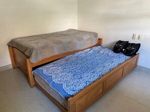 Un letto singolo con struttura in legno, una coperta grigia e una trapunta azzurra con motivo decorativo. Sulla testiera, due cuscini neri con un disegno di gatto.
