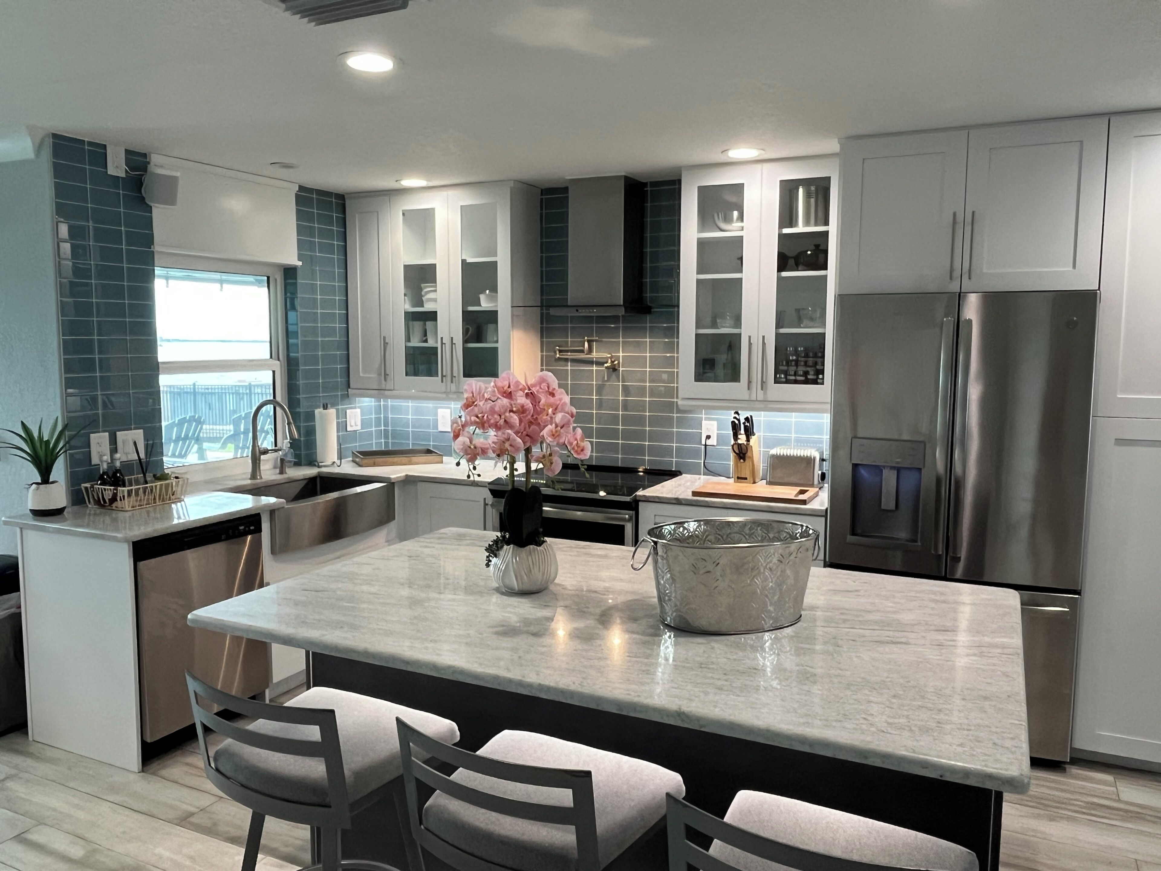 A modern kitchen with a central island, stainless steel appliances, and a view to the outside.