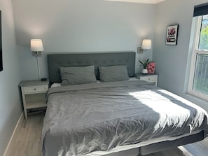 A bedroom with a bed, two bedside tables, a nightstand, a window, and a wall-mounted picture. - Beautiful Home (Cape Coral)