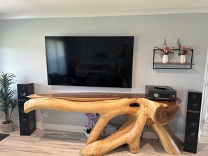 A wooden console table with a flat-screen TV mounted above it, flanked by two speakers, and a small shelf with decorative items. - Beautiful Home (Cape Coral)